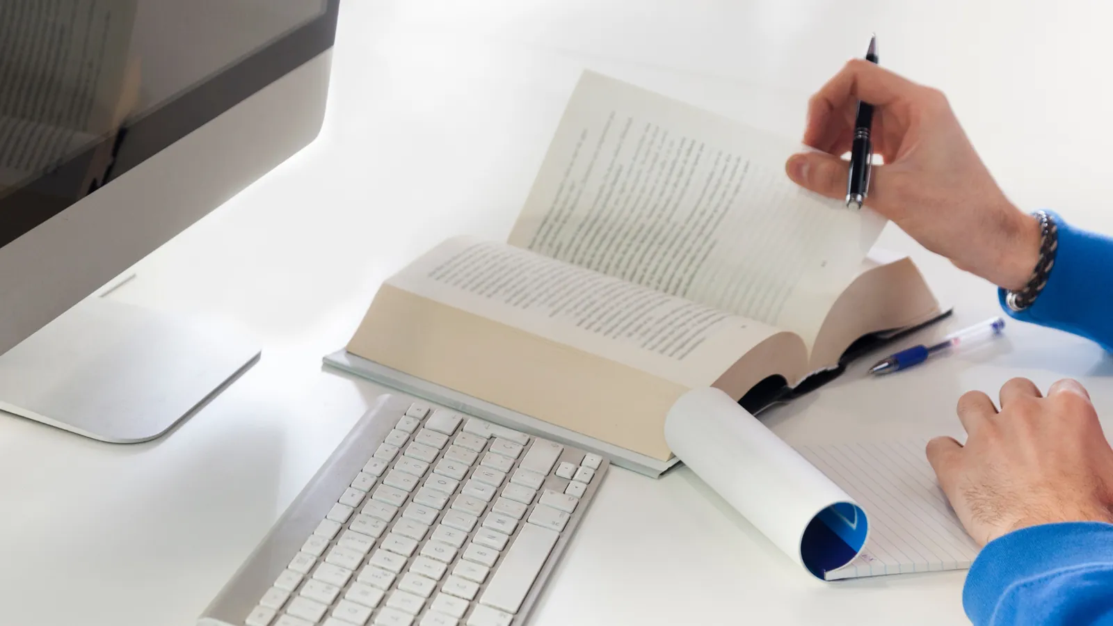 Personne qui consulte un livre et prend des notes devant un ordinateur