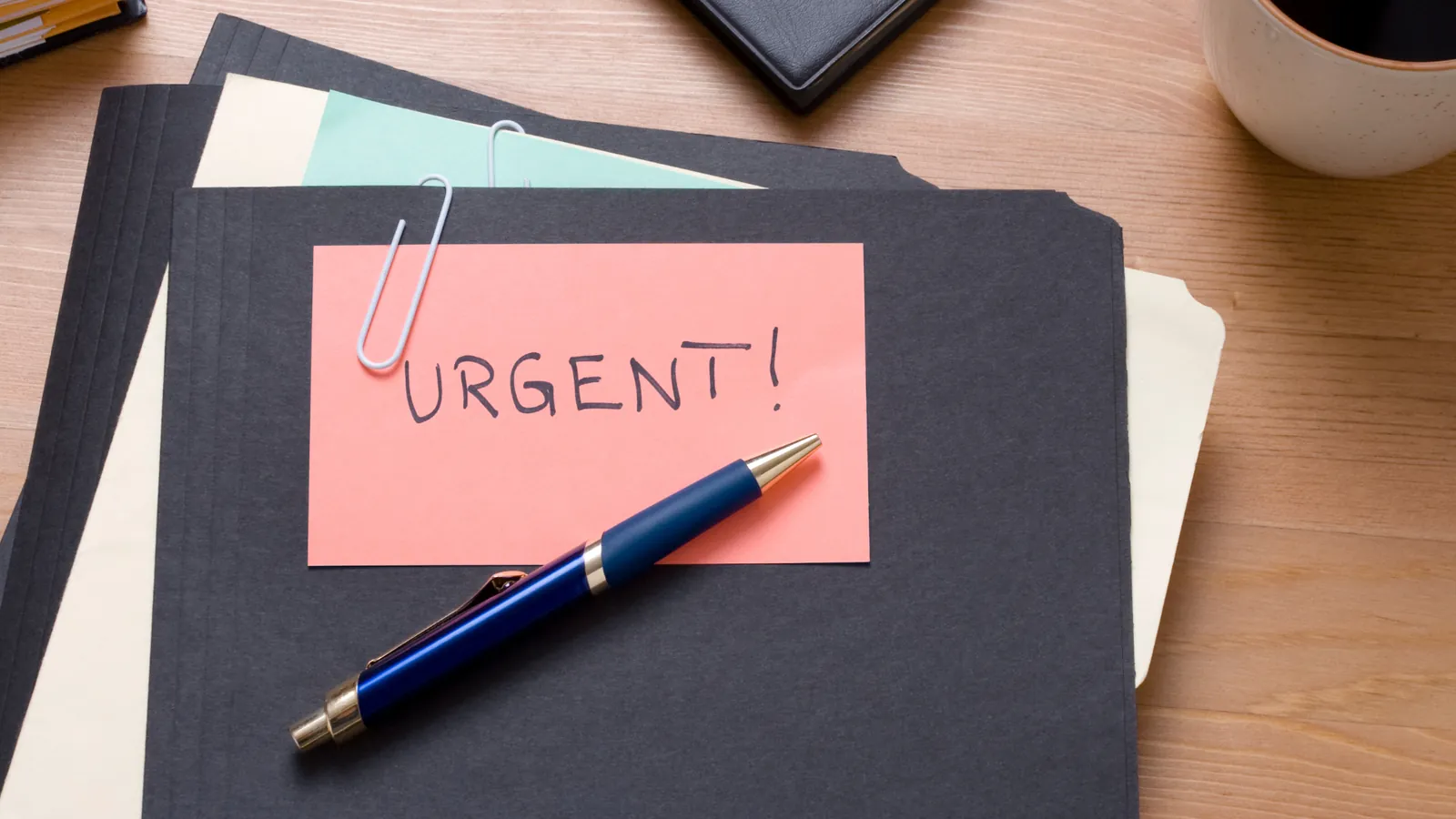 Note « urgent » posée sur des dossiers, avec un stylo